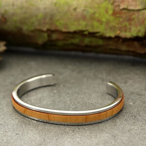 Peut inclure: Un bracelet jonc en argent avec une fine bande d'incrustation en bois. Le bois est de couleur brun clair.