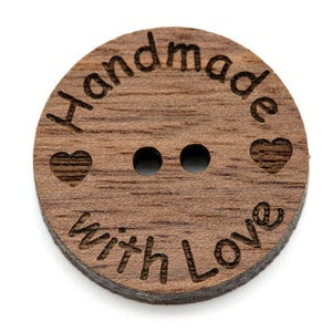 Puede incluir: Un botón redondo de madera con dos agujeros. El botón es marrón y tiene el texto "Handmade with Love" grabado en él. Hay dos pequeños corazones a cada lado del texto.