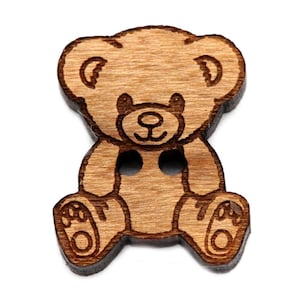 Può includere: Un bottone di legno a forma di orsacchiotto. Il bottone è marrone e ha un design semplice con due fori per cucire.
