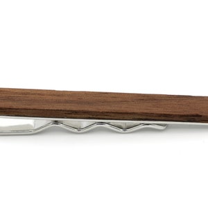 Könnte beinhalten: Ein brauner Holz-Krawattenclip mit einem silbernen Metallverschluss. Der Krawattenclip ist etwa 5 cm lang.