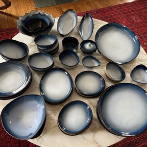 May include: A collection of blue and white ceramic tableware, including plates, bowls, and serving dishes. The pieces have a gradient effect, transitioning from a dark blue rim to a white center. Various shapes and sizes are displayed on a round table.