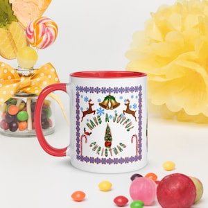 Könnte beinhalten: Weißer Keramikbecher mit rotem Innenraum und Henkel. Der Becher hat ein festliches Design mit dem Text "Have a Joyful Christmas", Rentieren, Glocken, Schneeflocken und Zuckerstangen. Der Becher ist von bunten Süßigkeiten und einer gelben Papierblume umgeben.