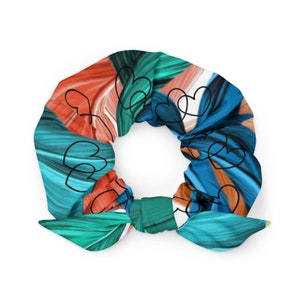 Puede incluir: Una colorida scrunchie con un vibrante patrón de tonos turquesa, naranja y azul. El diseño incluye corazones negros dibujados a trazos. La scrunchie tiene un lazo liso turquesa, que añade un toque elegante a este accesorio para el cabello.