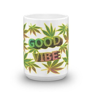 Peut inclure: Mug en céramique blanche avec un motif de feuilles de cannabis et l'inscription "GOOD VIBE" en lettres colorées. Les feuilles sont vertes, jaunes et rouges.