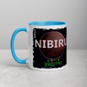 May include: A white ceramic mug with a light blue handle and interior. The mug features the word "NIBIRU" in white, with a red and black planet graphic. Text below reads "Keep your eyes to the heavens and look out for the signs of what is to come."