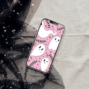 May include: A smartphone displays a pink background with white cartoon ghosts, green sprigs, and orange stars. The phone is on a neutral-colored surface next to black tulle with gold stars.