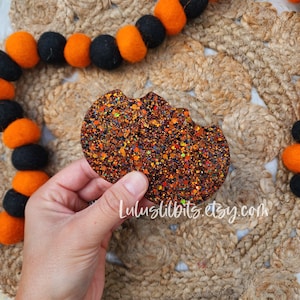 May include: A glittery orange and brown pumpkin shaped cutout with a bite taken out of it. The cutout is made of resin and has a sparkly finish.