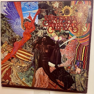 Puede incluir: Portada del álbum para el álbum Abraxas de Santana. La obra de arte presenta un collage vibrante con una figura roja con alas, una mujer de piel oscura, una paloma blanca y el título del álbum en escritura roja. El fondo incluye un tambor, flores y patrones coloridos.