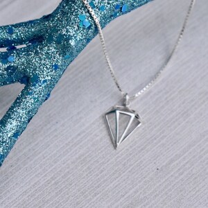 May include: A silver chain necklace with a geometric diamond pendant.