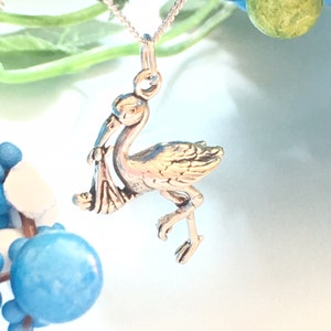 May include: Silver stork charm necklace featuring a baby in its beak. The charm is detailed and has a realistic look. The necklace is a great gift for a new parent.