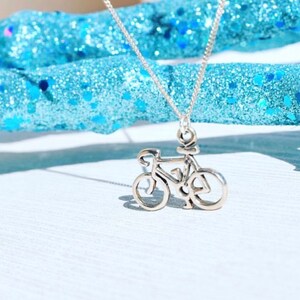May include: A silver necklace featuring a delicate bicycle pendant. The pendant is a simple outline of a bicycle with thin lines.