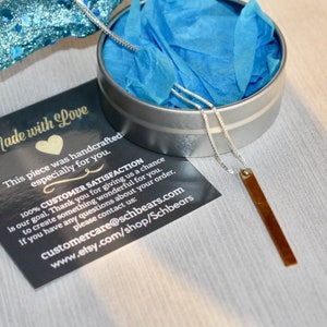 May include: A silver chain necklace with a brown rectangular pendant. The necklace is packaged in a silver tin with blue tissue paper. The tin has a black card with the text "Made with Love. This piece was handcrafted especially for you. 100% CUSTOMER SATISFACTION is our goal. Thank you for giving us a chance to create something wonderful for you. If you have any questions about your order, please contact us: customercare@schbears.com www.etsy.com/shop/Schbears"
