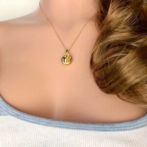 May include: A gold chain necklace with a small, round, gold pendant. The pendant has a textured, intricate design.