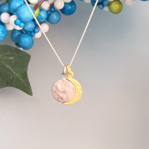May include: A silver necklace with a hammered silver circle pendant and a gold crescent moon charm.