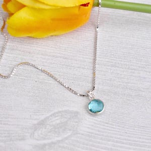 May include: A silver chain necklace with a small, round, light blue gemstone pendant.
