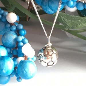 May include: A silver necklace with a football charm. The charm is detailed with a textured surface and a classic football design.