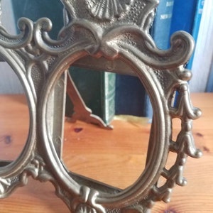 May include: A vintage brass picture frame with ornate details and a decorative design. The frame has two oval openings and a stand on the back.