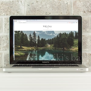 May include: A laptop computer displaying a website with the text "kiki's bay" and a photo of a lake and mountains. The website is for a business called "kiki's bay".