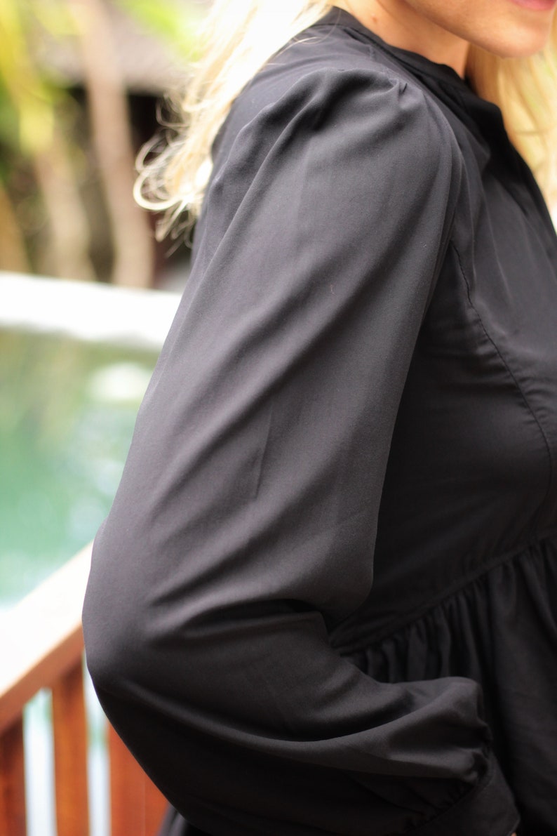 May include: A black long-sleeved blouse with a gathered waist and puffed sleeves.