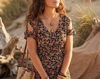 Könnte beinhalten: Ein schwarzes Kleid mit kleinem orangefarbenem und grünem Blumenmuster, kurzen Ärmeln mit Schulterausschnitten und V-Ausschnitt. Das Kleid wird mit einer geflochtenen Stroh-Beuteltasche mit braunen Lederriemen, geschichteten Steinketten und Armreifen kombiniert.