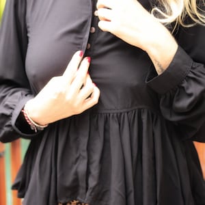 May include: A black, long-sleeved blouse with a ruffled hem and a button-up front. The blouse is worn over a leopard print skirt.