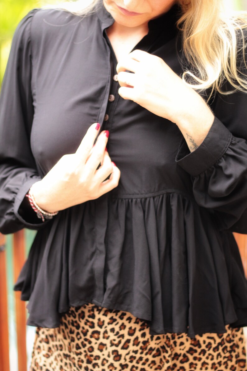 May include: A black, long-sleeved blouse with a ruffled hem and a button-up front. The blouse is worn over a leopard print skirt.