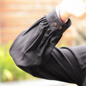 May include: Black long-sleeved shirt with a gathered puff sleeve and two buttons on the cuff.