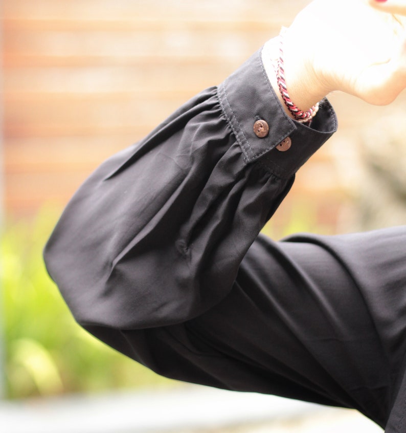 May include: Black long-sleeved shirt with a gathered puff sleeve and two buttons on the cuff.