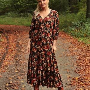 Könnte beinhalten: Eine Frau in einem langen, schwarzen Blumenkleid mit braunen Stiefeln. Sie steht auf einem Weg in einem Wald mit heruntergefallenen Blättern.