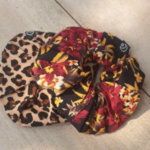 Könnte beinhalten: Ein schwarzes Haargummi mit einem Blumenmuster auf der einen Seite und einem Leopardenmuster auf der anderen Seite.