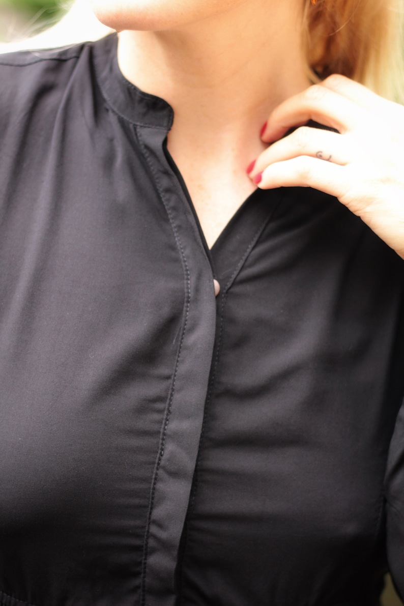 May include: A close-up of a black button-up shirt with a single button fastened at the collar.