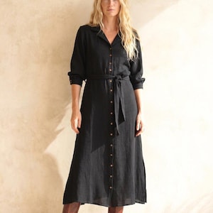Könnte beinhalten: Schwarzes Midikleid mit langen Ärmeln, Knopfleiste vorne und passendem Bindegürtel. Das Kleid hat einen Kragen und ist aus einem strukturierten Stoff gefertigt. Ein vielseitiges Kleidungsstück für verschiedene Anlässe.