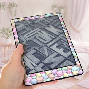 May include: An e-reader with a colorful macaron pattern border. The screen displays a close-up of gray letterpress printing blocks. The e-reader is held in a hand, with a soft, pastel-colored background.