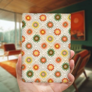 May include: A close-up of a crocheted blanket with a white background and a repeating pattern of orange, green, and yellow flowers.