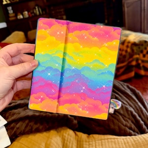 May include: A square e-reader cover featuring a vibrant rainbow-colored cloud pattern. The design displays layers of pink, orange, yellow, green, blue, and purple clouds with a subtle glittery texture and small white star-shaped sparkles throughout.