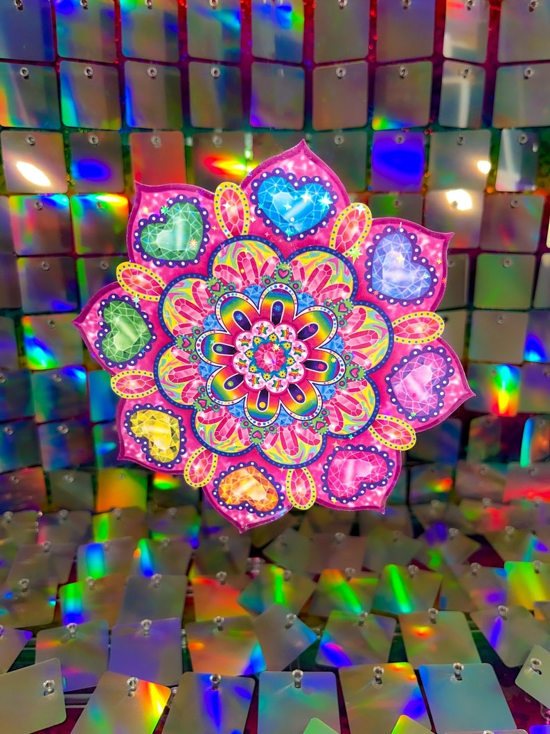 May include: A pink and rainbow mandala with hearts and jewels. The mandala is against a background of iridescent sequins.