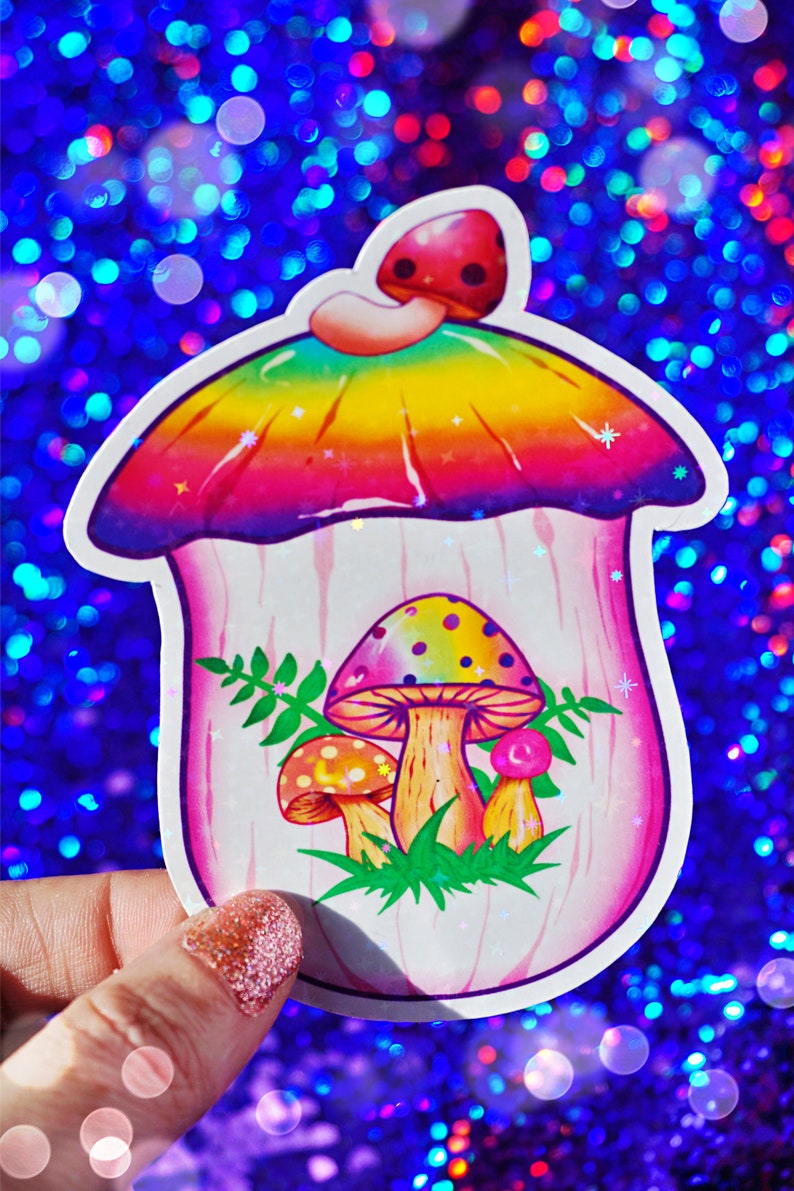 May include: A colorful mushroom sticker with a rainbow-colored top and a pink body. The sticker features three smaller mushrooms inside, with green leaves and a white outline. The background is a sparkly blue.
