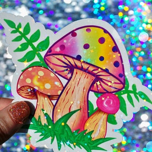 May include: A colorful sticker featuring three stylized mushrooms with rainbow-colored caps and dotted patterns. The sticker includes green foliage and is set against a sparkly, iridescent background.