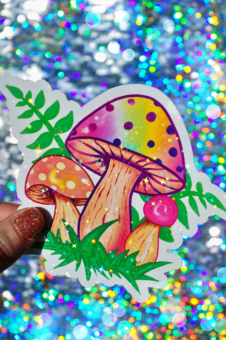 May include: A colorful sticker featuring three stylized mushrooms with rainbow-colored caps and dotted patterns. The sticker includes green foliage and is set against a sparkly, iridescent background.