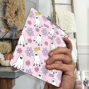 May include: A pink and white patterned square coaster with a repeating design of white ghosts and purple flowers with the word "BOO!" in yellow letters.