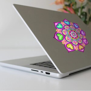 May include: A silver laptop with a colorful mandala sticker on the back. The mandala features a pink, yellow, green, and blue design with hearts around the edges.