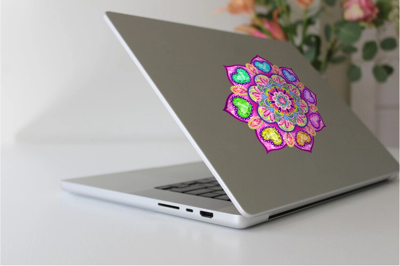 May include: A silver laptop with a colorful mandala sticker on the back. The mandala features a pink, yellow, green, and blue design with hearts around the edges.
