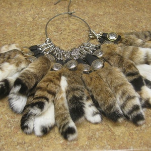 May include: A collection of brown, black, and white faux fur keychains with silver key rings and decorative metal charms. The keychains are attached to a metal ring.