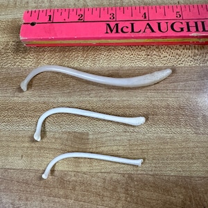 May include: Three white plastic or ceramic curved pieces on a wood surface. The pieces are approximately 3 inches long.