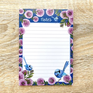 May include: A blue notepad with a floral border featuring pink flowers and blue birds. The notepad has lined paper and the word "Notes" printed at the top.