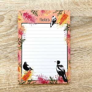May include: A pink notepad with a floral border featuring black and white birds and the word "Notes" at the top. The notepad has lined paper for writing.