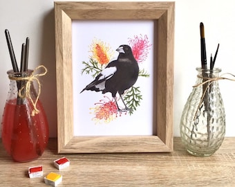 May include: A framed print of a black and white magpie bird perched on a branch with pink and yellow flowers. The print is in a light wood frame.