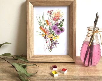 Puede incluir: Una impresión enmarcada de una pintura de acuarela de un ramo de flores nativas australianas. Las flores son en tonos de rosa, amarillo, naranja y morado. La impresión está en un marco de madera.