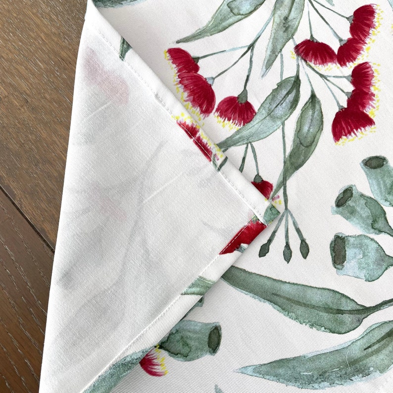May include: A white table runner with a watercolor design of red gum blossoms and green eucalyptus leaves.
