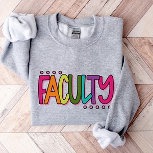 Może przedstawiać: Szara bluza z nadrukiem słowa "FACULTY" w kolorach tęczy. Litery są obwiedzione czarną ramką i mają biały cień.